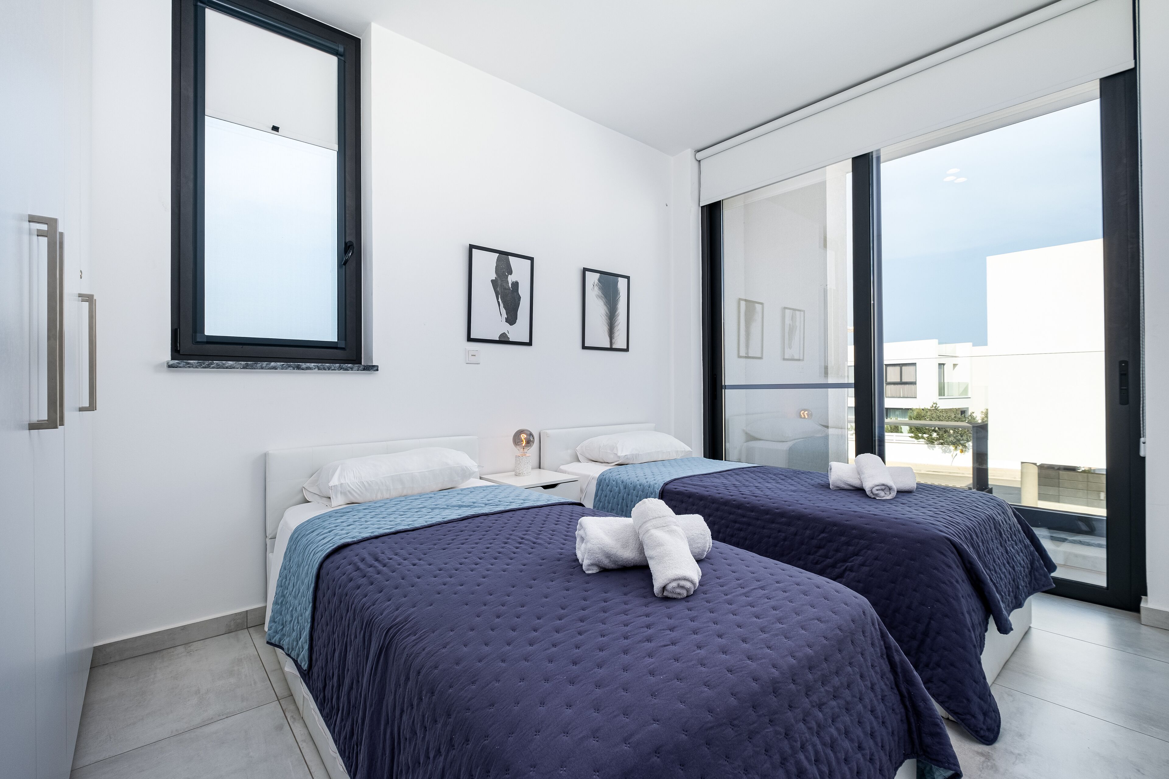 A modern hotel room with two beds, a large window, and artwork on the wall.