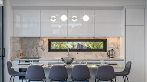 Uma cozinha moderna com armários brancos, bancada de mármore e uma área de jantar com quatro cadeiras.