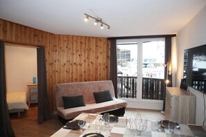 A cozy living room with a sofa, a dining table set for two, and a TV mounted on the wall.
