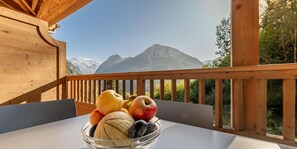 A wooden balcony with a table holding a bowl of fruit and a mountain view. - 2nd floor, fitness, swimming pool, sauna, hammam, terrace, parking, tv, 58m², Champagny-en-Vanoise (Champagny-en-Vanoise)