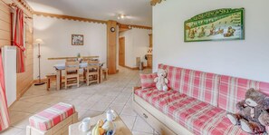 A cozy living room with a plaid sofa, a dining table with chairs, a wooden bench, and a teddy bear.