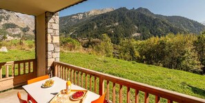 A balcony with a table set for dining, overlooking a mountainous landscape.