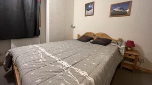 A bedroom with a bed, two wall-mounted pictures, a nightstand with a lamp, and a window with a curtain. - 180m from ski slopes, floor -1, view mountain, balcony, tv, 37m², Méribel-Mottaret (Méribel - Les Allues)