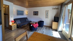 A cozy living room with a sofa, a small table, and a TV stand. - 180m from ski slopes, floor -1, view mountain, balcony, tv, 37m², Méribel-Mottaret (Méribel - Les Allues)