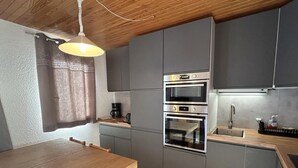 A compact kitchen with grey cabinets, a wooden table, and a built-in oven. - 180m from ski slopes, floor -1, view mountain, balcony, tv, 37m², Méribel-Mottaret (Méribel - Les Allues)