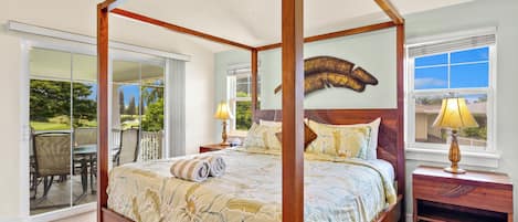 A four-poster bed with a floral bedspread, a ceiling fan, and a view of a patio with outdoor furniture.