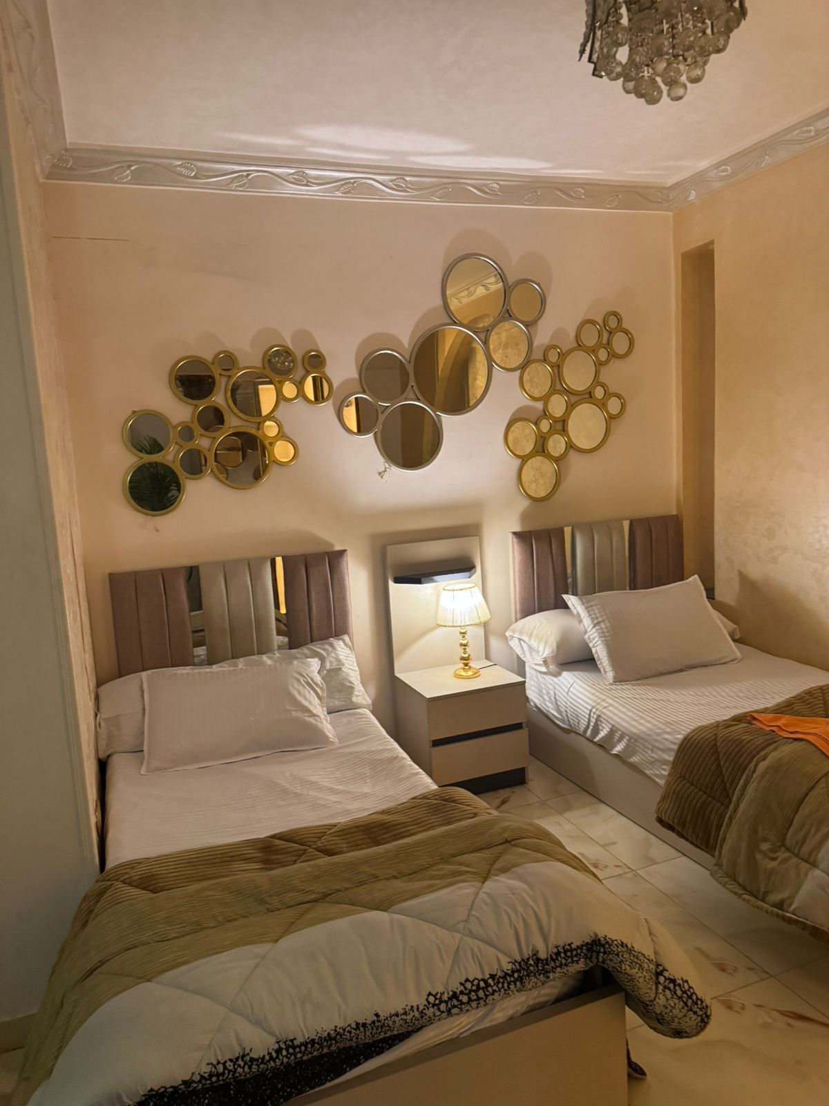 A hotel room with two beds, a wall-mounted mirror arrangement, and a chandelier.