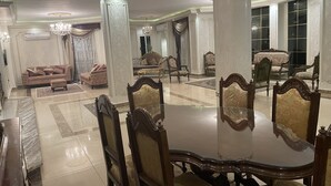 A spacious dining area with a large table surrounded by ornate chairs, a chandelier, and classical columns. - Fancy 3 bedrooms  240 m apartment in sheik zayed compound (6th of october)