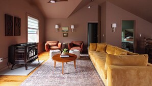 A spacious living room with a large sofa, two armchairs, a coffee table, and a vintage stove. - Charming Cavendish Guesthouse (Cavendish)