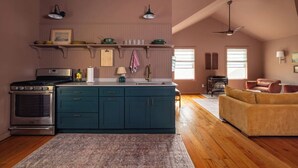 A kitchen with teal cabinets, a stove, and a sink. There is a wooden floor and a rug. - Charming Cavendish Guesthouse (Cavendish)