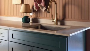 A kitchen with a wooden panel backsplash, a sink with a brass faucet, and a teal cabinet with gold handles. - Charming Cavendish Guesthouse (Cavendish)