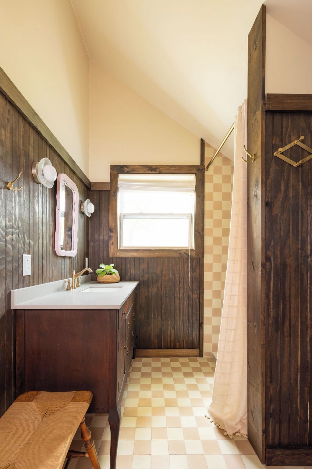 A compact bathroom with a wooden vanity, a small window, a shower curtain, and a bench.