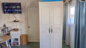 A room with a television mounted on the wall, a wardrobe, a small table with a chair, and a trash bin. - Studio Lighthouse, Walking - 10 min to the beach (Noord)