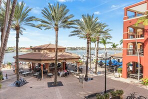 A waterfront patio with outdoor seating, palm trees, and a building with balconies.