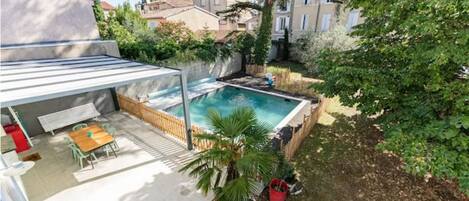 A covered patio with a pool, surrounded by greenery and residential buildings.