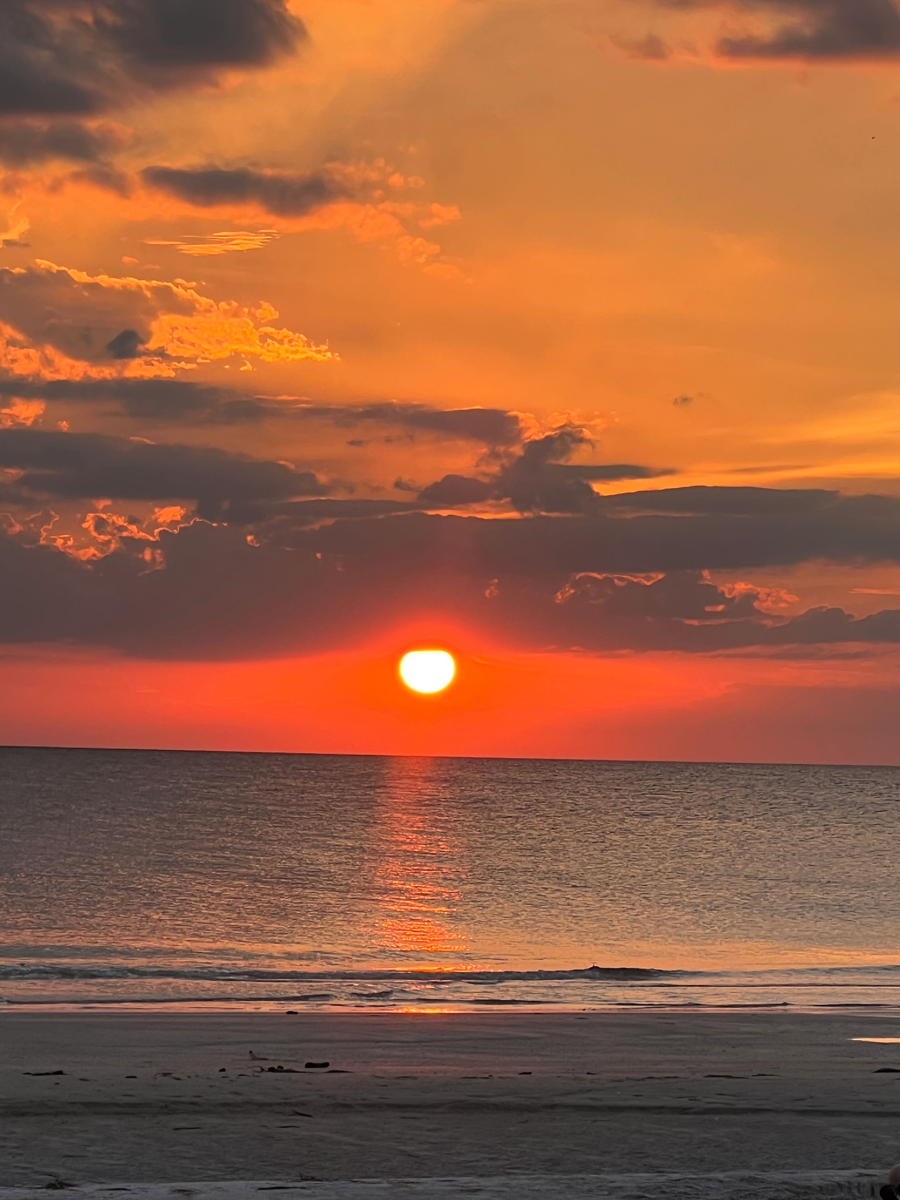 Ein Sonnenuntergang über dem Meer mit Wolken, die das Sonnenlicht reflektieren.