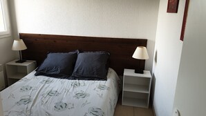 Un dormitorio con cabecera de madera, dos mesitas de noche con lámparas, una cama con edredón blanco estampado con flores y una pared lisa.