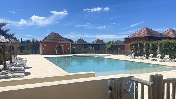 Una piscina con sillas de descanso, un edificio pequeño y casas con tejados rojos.