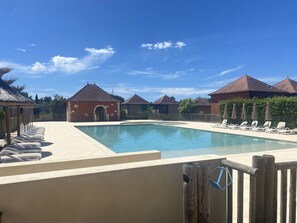 En swimmingpool med solstolar, en liten byggnad och hus med röda tak.