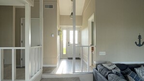 Un vaste espace de vie avec un canapé gris, un escalier menant à une autre pièce et un couloir se terminant par une porte.