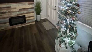 A living room with a fireplace, a television, and a Christmas tree.