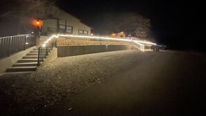 A nighttime view of a building with a staircase leading up to a gated entrance, surrounded by a gravel area.