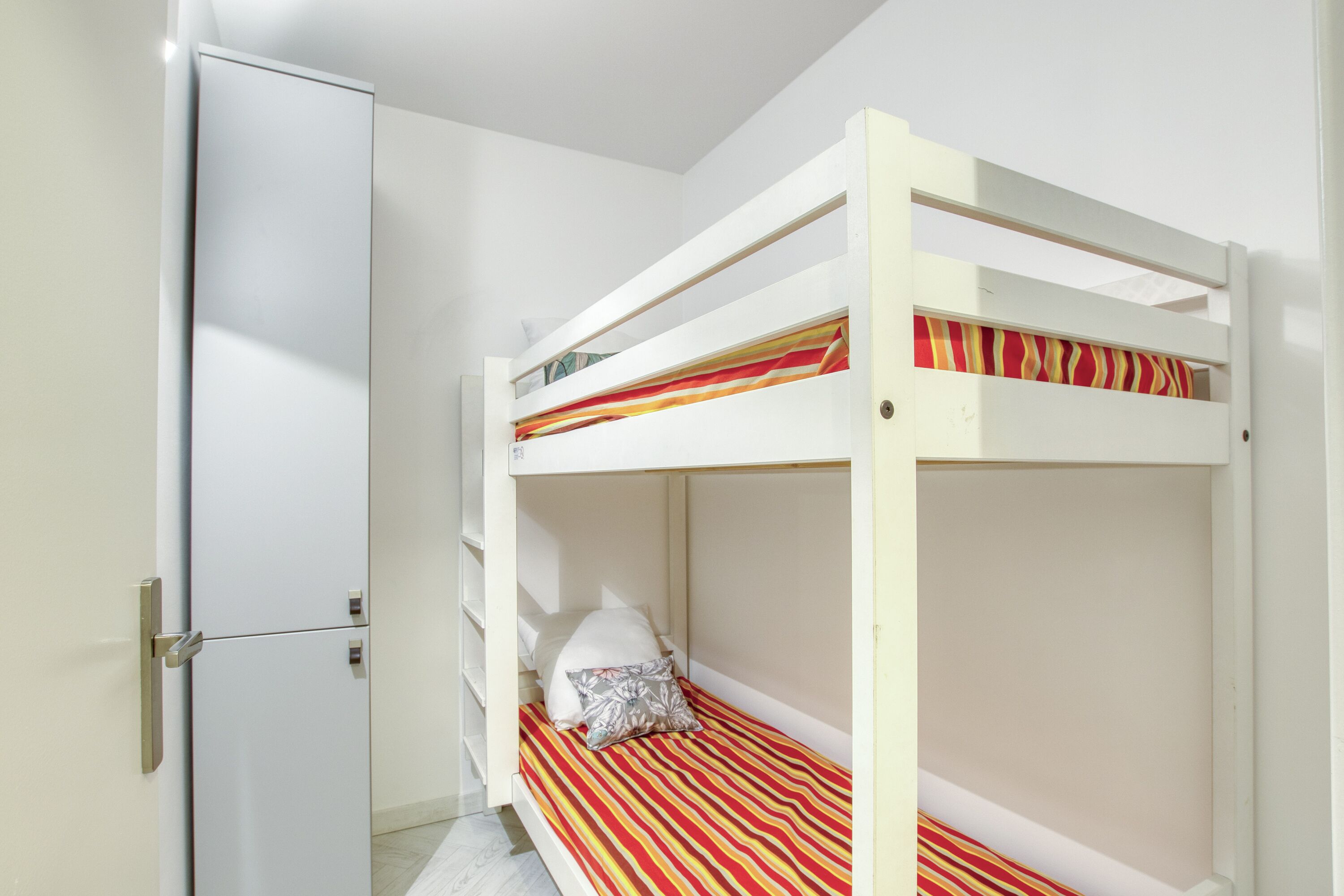 Uma cama beliche com colchão listrado, um guarda-roupa branco e uma porta com puxador.