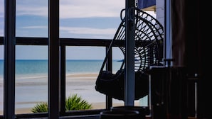 A view of a beach through large windows, a hanging chair, and a potted plant.