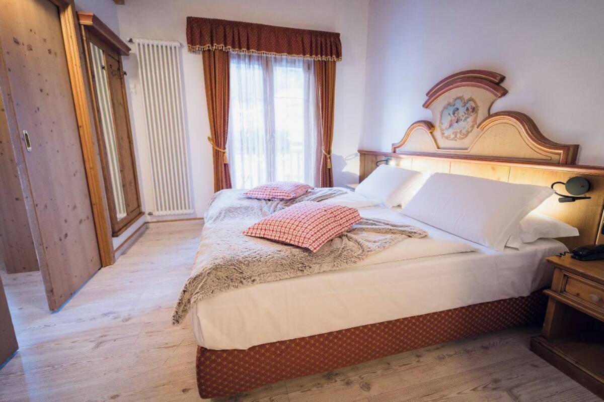 Une chambre avec un lit en bois, une table de chevet, un radiateur et une fenêtre avec des rideaux.
