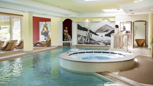 Une piscine intérieure dotée d’un jacuzzi, de chaises longues et d’une fresque murale.