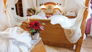 Un lit en bois avec une literie blanche et un baldaquin, un vase rempli de fleurs et une petite table recouverte d’une nappe en dentelle.