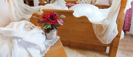A wooden bed with white bedding and a canopy, a vase with flowers, and a small table with a lace tablecloth.