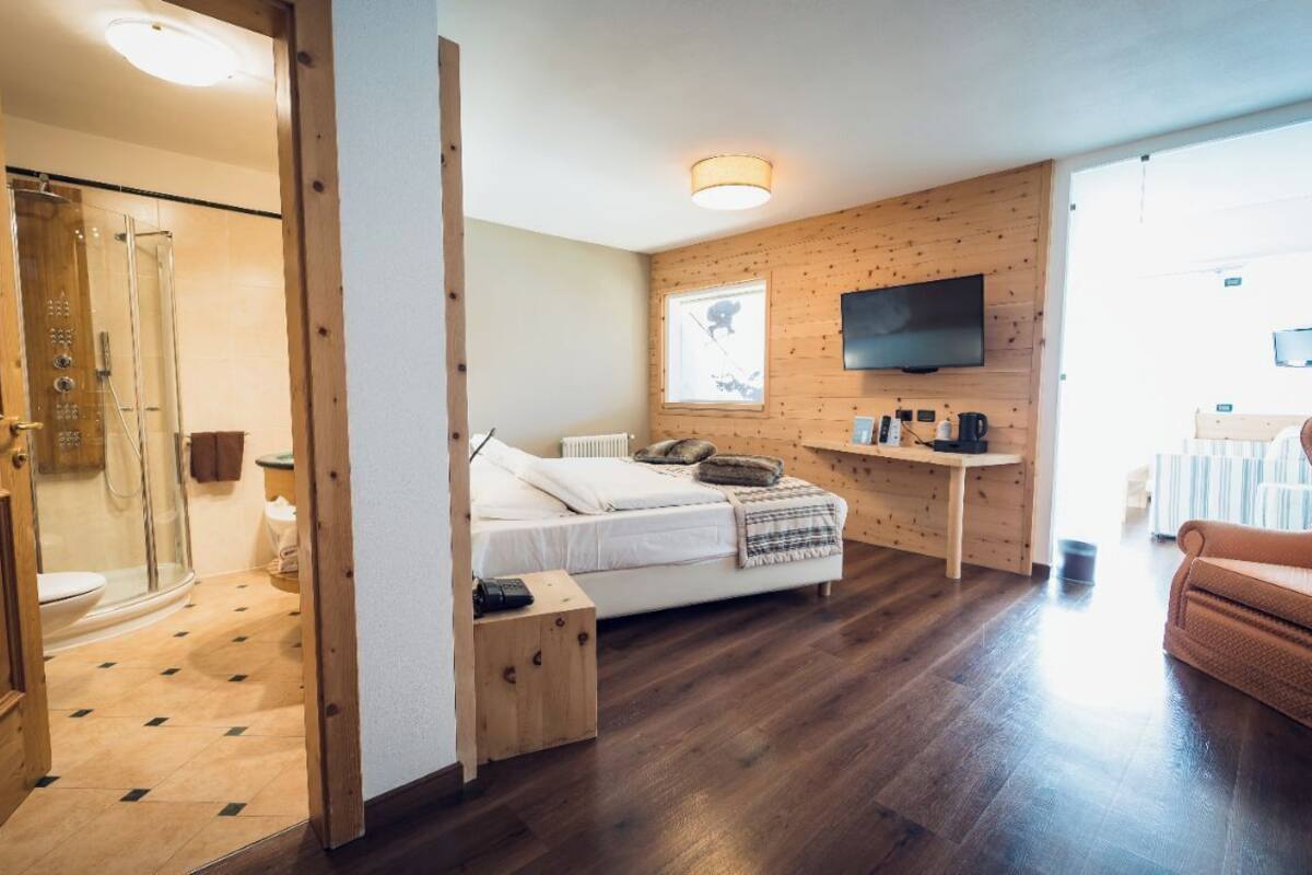 Une chambre d’hôtel moderne avec un plancher en bois, un lit avec télévision, un petit bureau et une douche.