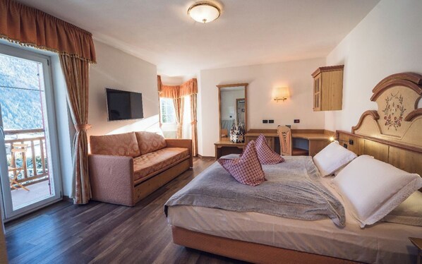 A bedroom with a bed, a sofa, a desk, and a TV. - Renato Hotel (San Giovanni di Fassa)
