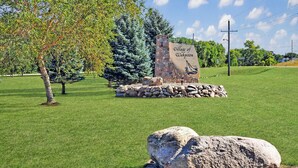 A stone sign with "Village of Washington" inscribed, surrounded by a grassy area with trees and a clear sky.