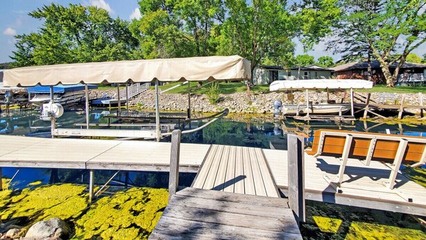 A wooden dock leading to a clear swimming pool with a wooden deck and a canopy.