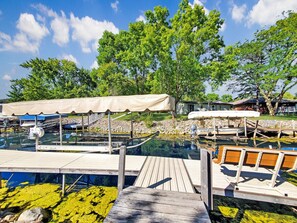 A wooden dock leading to a clear swimming pool with a wooden deck and a canopy.