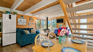 A cozy kitchen with a wooden ceiling, a teal sofa, and a dining table set with blue plates and a vase of flowers. - Blue Pearl MCA#278-Perfect couples retreat. Dogs welcome, 4 blocks to beach (Manzanita)