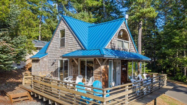 A wooden cabin with a blue roof, a deck with chairs, and a covered porch. - Blue Pearl MCA#278-Perfect couples retreat. Dogs welcome, 4 blocks to beach (Manzanita)