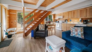 A wooden interior with a staircase, a kitchen, a blue sofa, and a wicker table. - Blue Pearl MCA#278-Perfect couples retreat. Dogs welcome, 4 blocks to beach (Manzanita)
