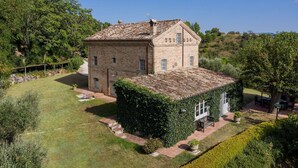 A two-story stone building with a tiled roof, surrounded by a well-maintained garden and a clear sky. - Casa Antonio - Private villa, 4 bedrooms, pool, A/C, wifi, pets, Marche (Mogliano)
