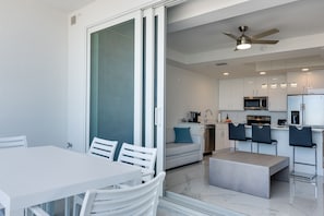 Cocina moderna con armarios blancos, microondas y refrigerador. Hay un comedor con mesa y sillas blancas.