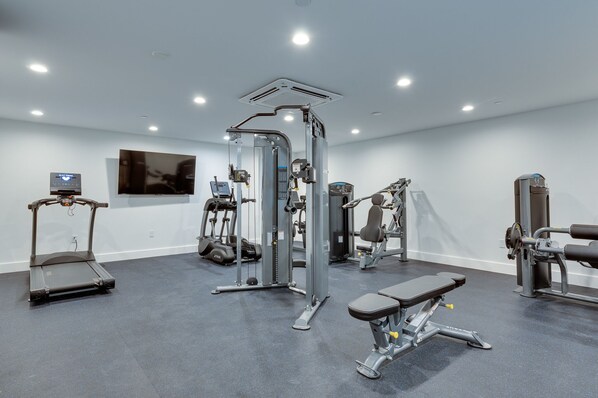 Ein modernes Fitnessstudio mit verschiedenen Trainingsgeräten, darunter Laufband, Kraftgeräte und eine Bank.