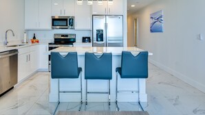 Een moderne keuken met witte kasten, roestvrijstalen apparatuur en een centraal eiland met barstoelen.
