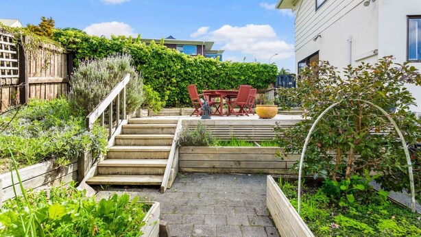 A garden with a wooden staircase leading to a patio area with a table and chairs. - Coastal Retreat Unit close to Beach (Auckland North Shore)