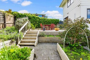 A garden with a wooden staircase leading to a patio area with a table and chairs. - Coastal Retreat Unit close to Beach (Auckland North Shore)