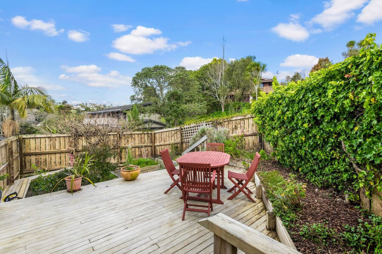 A wooden deck with a round table and chairs, surrounded by a wooden fence and lush greenery.