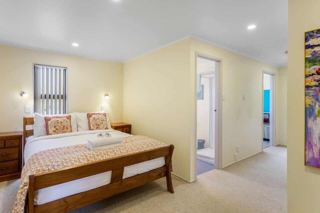 A bedroom with a wooden bed, a nightstand, a wall-mounted light, and a door leading to another room.
