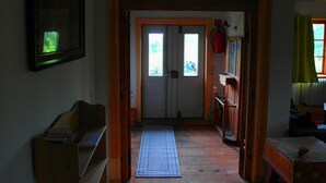 Un pasillo con una puerta de madera, un felpudo y una estantería con un objeto rojo.