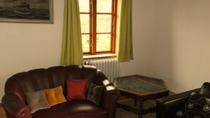 Una habitación con un sillón de cuero, una mesita, un radiador y una ventana con cortinas.